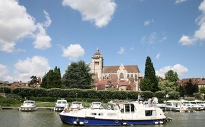 Boats dock along the serene riverbank, surrounded by lush greenery and a historic church in the background.