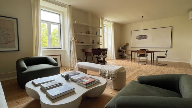 A living room with a sofa, a coffee table with books, a desk with a chair, and a large window with curtains. - Eco Luxury apartment Campo de Ourique LISBON center (Lisboa)