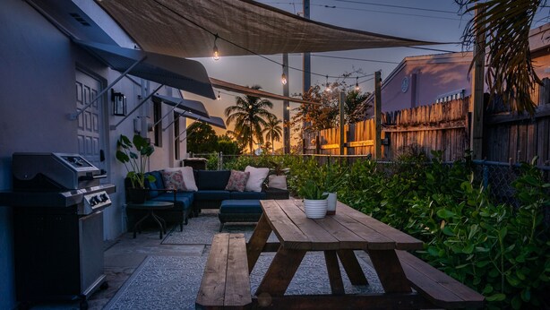An outdoor patio with a wooden table, a sofa, and a grill.