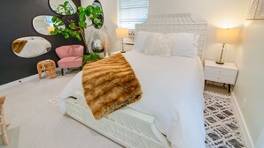 A modern bedroom with a white bed, a pink chair, a large mirror, and a plant.