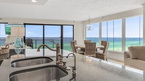 A modern kitchen with a large island, a dining area with wicker furniture, and a view of the ocean through large windows. - Beachfront Wraparound Balcony ~ Golf Cart ~ Pool (Miramar Beach)