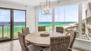 A dining area with a round table and wicker chairs, overlooking a beach and ocean. - Beachfront Wraparound Balcony ~ Golf Cart ~ Pool (Miramar Beach)