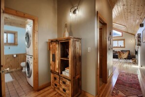 Un espace buanderie comprenant un lave-linge, un meuble en bois et un couloir menant à l’espace de vie.