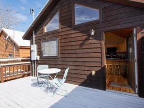 Een houten chalet met een terras, een eethoek met tafel en stoelen, en een keuken die door een open deur zichtbaar is.