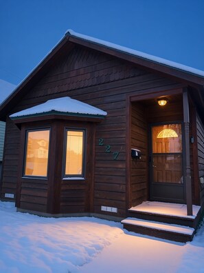 Een houten chalet met een donkerbruine buitenkant, een voordeur met een ruit en het cijfer 227 op de gevel.