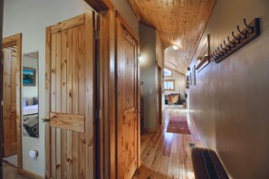 A wooden hallway with a ceiling fan, a wall-mounted coat rack, and a door leading to a room with a bed and a window. - The Little Lodge Leadville — 2BR with Hot Tub, Pet-OK, 1.5 Blocks to Harrison (Leadville)