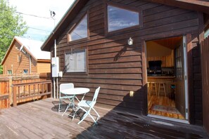 A wooden cabin with a deck, a dining area with chairs, and a kitchen visible through an open door. - The Little Lodge Leadville — 2BR with Hot Tub, Pet-OK, 1.5 Blocks to Harrison (Leadville)
