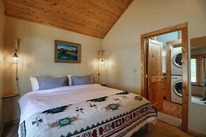 Een slaapkamer met een bed, een schilderij, een wasmachine en een houten plafond.