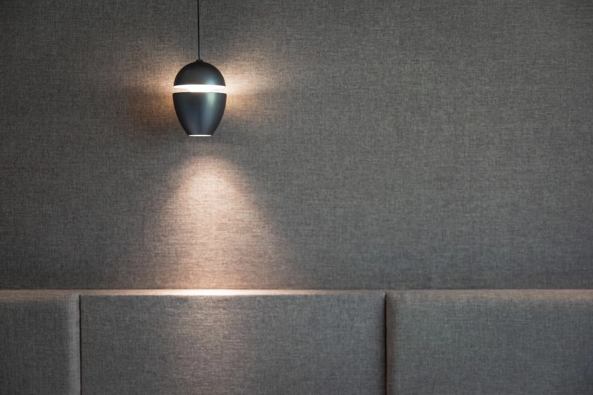 Una lámpara colgante con acabado metálico y un interior luminoso, instalada en una pared con textura.