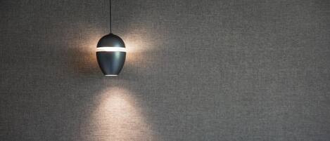 Una lámpara colgante con acabado metálico y un interior luminoso, instalada en una pared con textura.