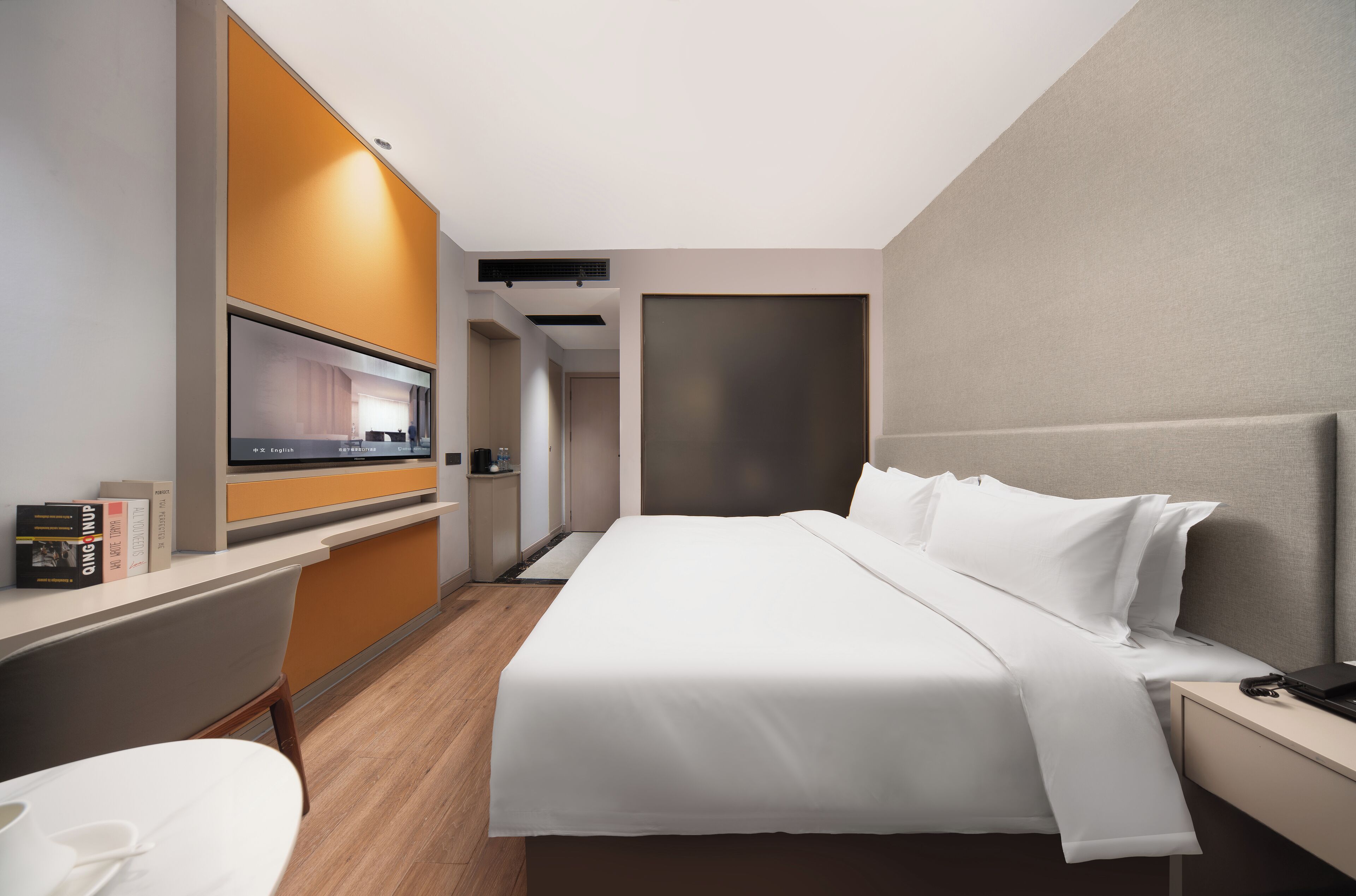 A modern hotel room with a large bed, a desk, and a small kitchenette.