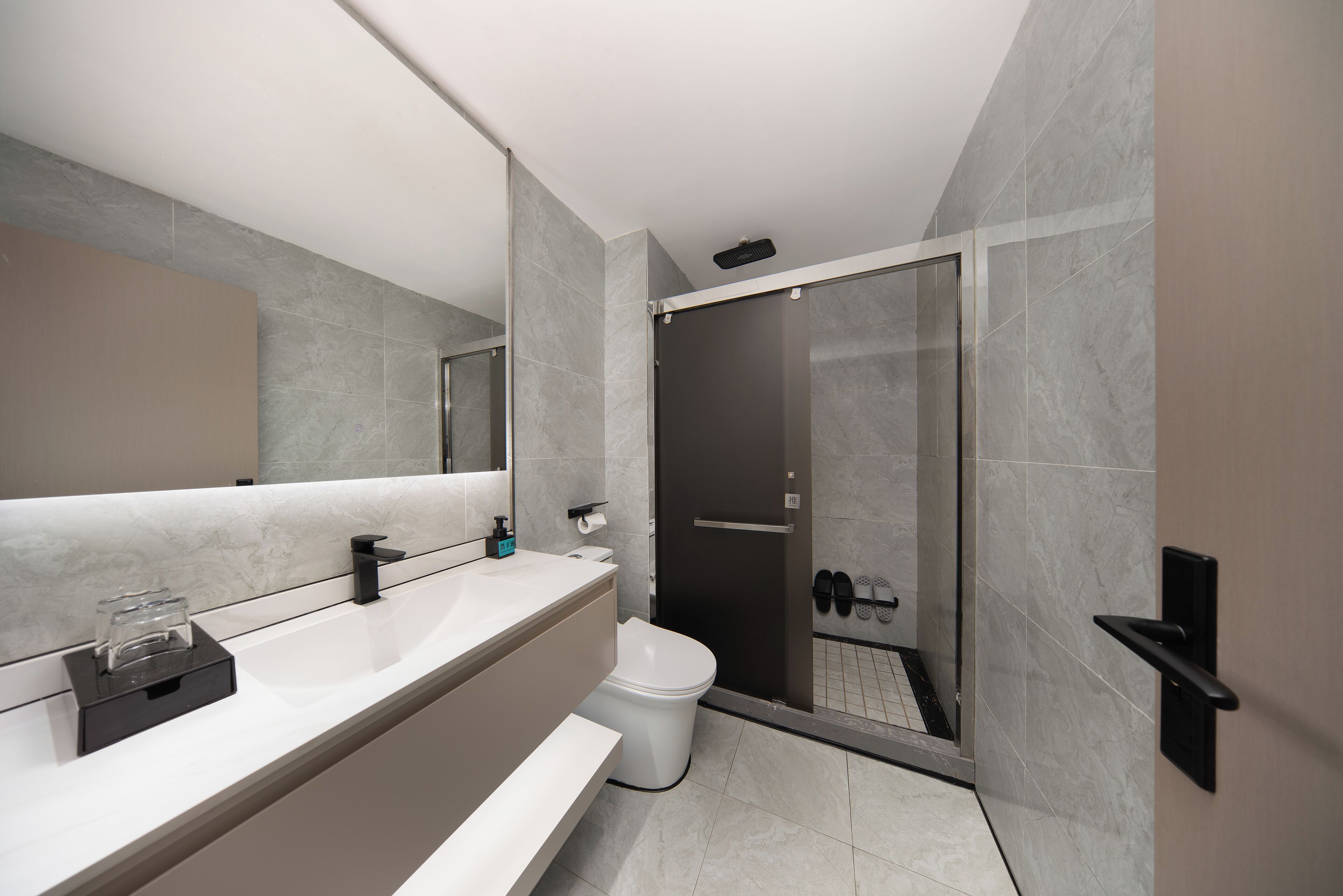 A modern bathroom with a large mirror, a white sink, a toilet, and a glass-enclosed shower area.