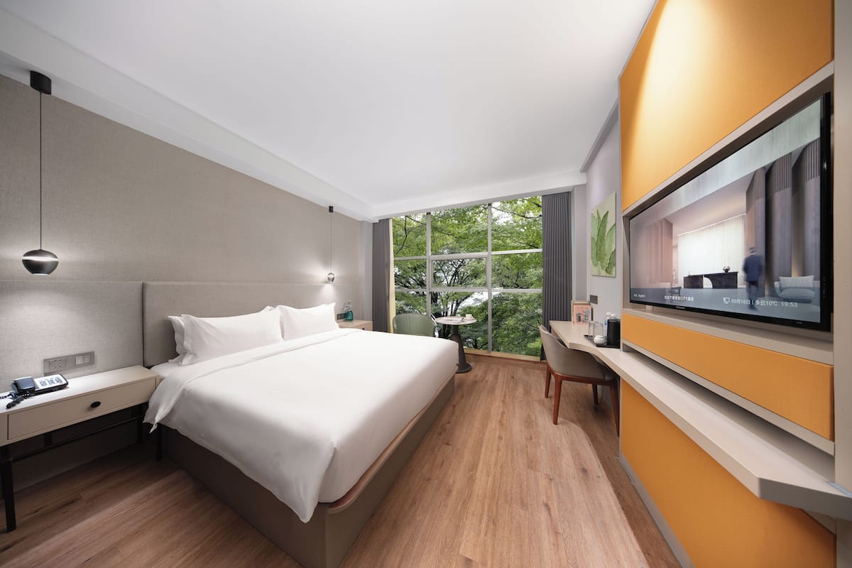 A modern hotel room with a large bed, bedside table with a phone, a desk with a chair, and a TV mounted on the wall.