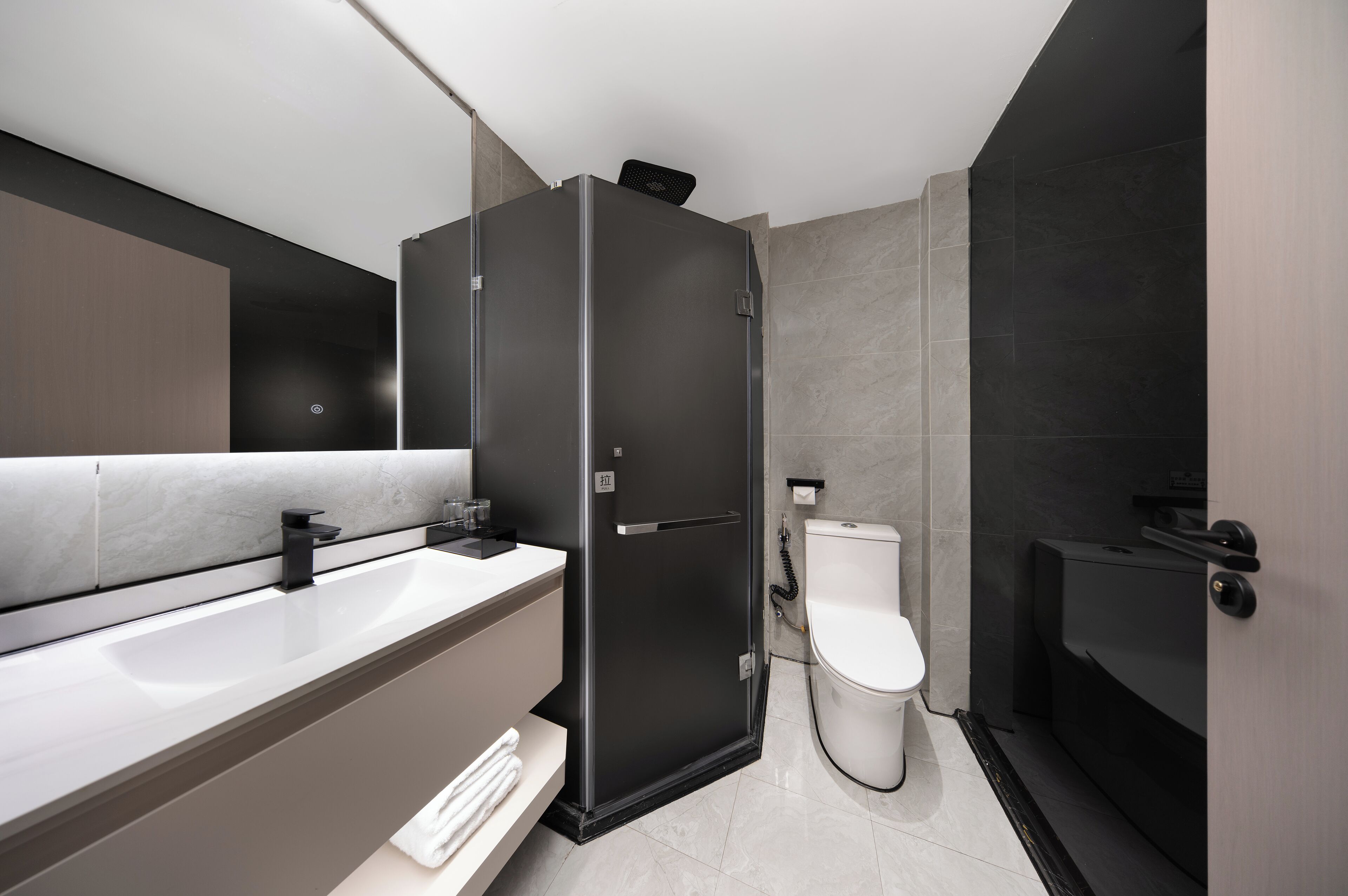 Un baño moderno con cabina de ducha negra, inodoro blanco y un espejo grande sobre el lavabo.