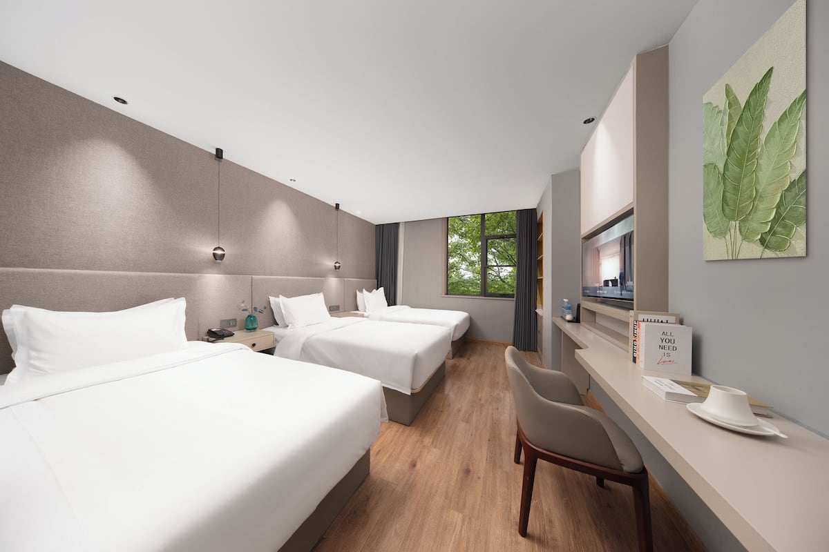 A hotel room with three beds, a desk, and a chair.