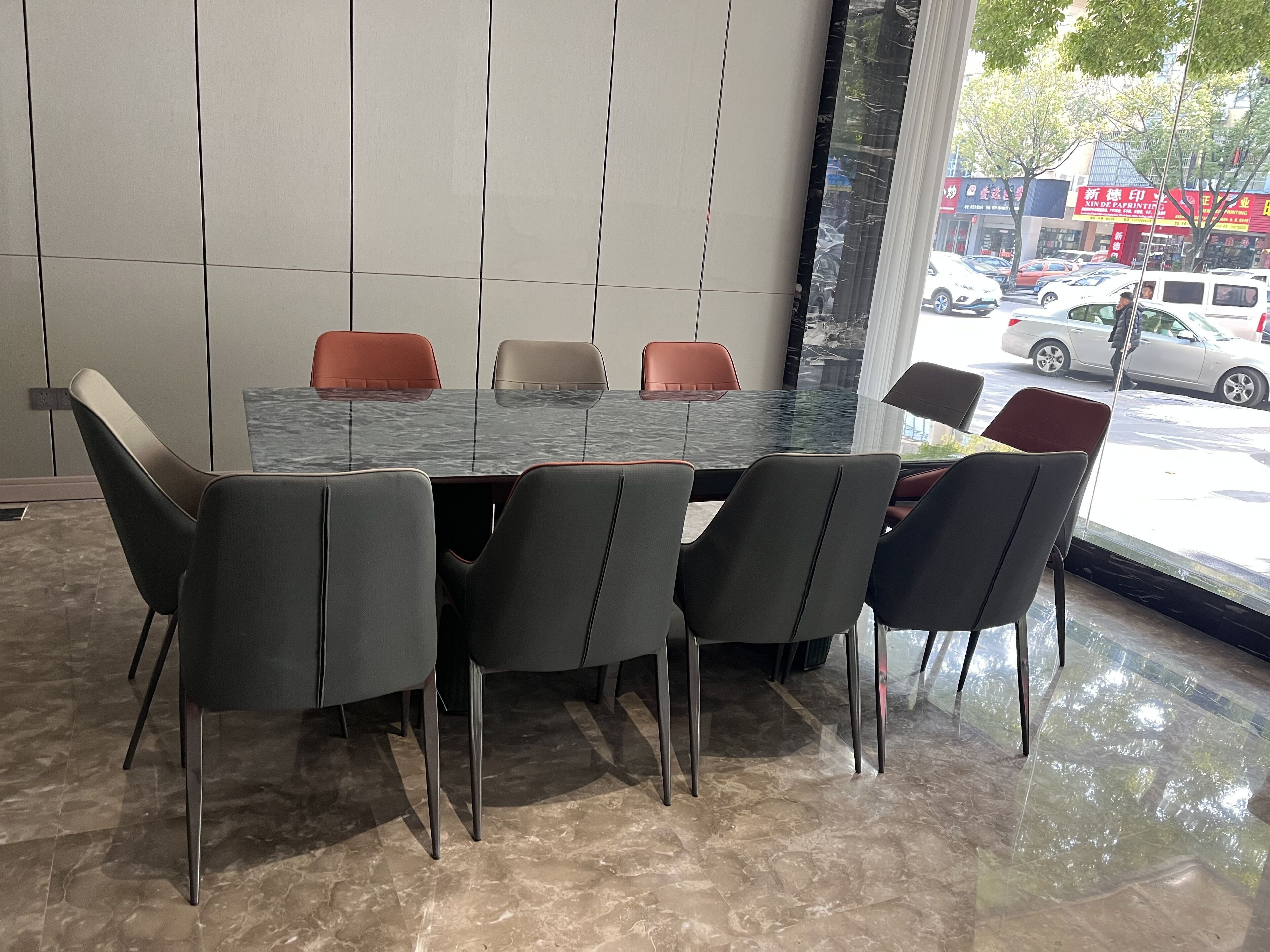 A conference room with a glass table, six chairs, and a view of the street through a large window.