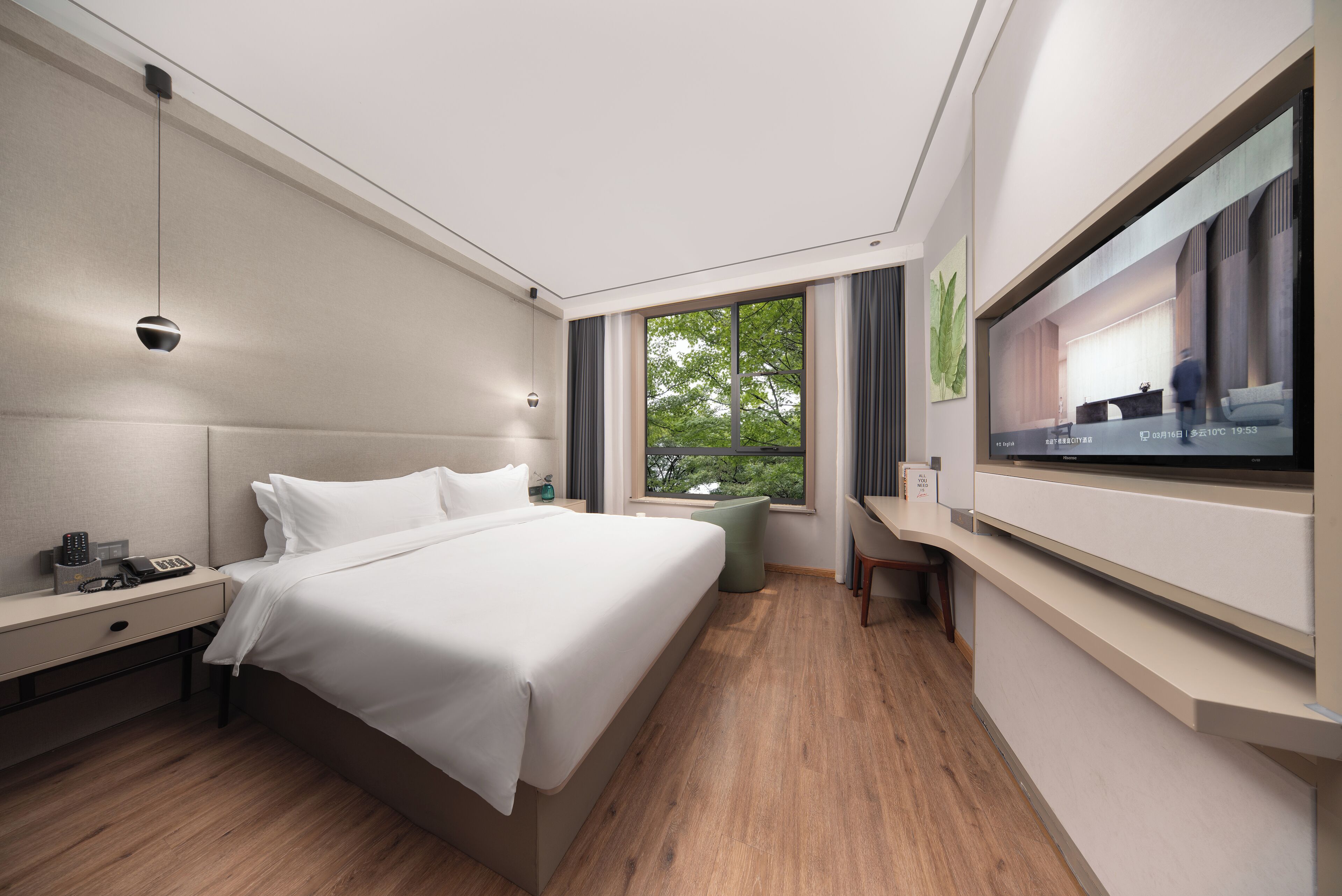 Une chambre d’hôtel moderne, dotée d’un grand lit, d’un bureau, d’une télévision et d’une fenêtre donnant sur un paysage verdoyant.