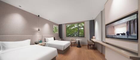 A modern hotel room with two beds, a small table, chairs, a TV, and a window with a view of trees.