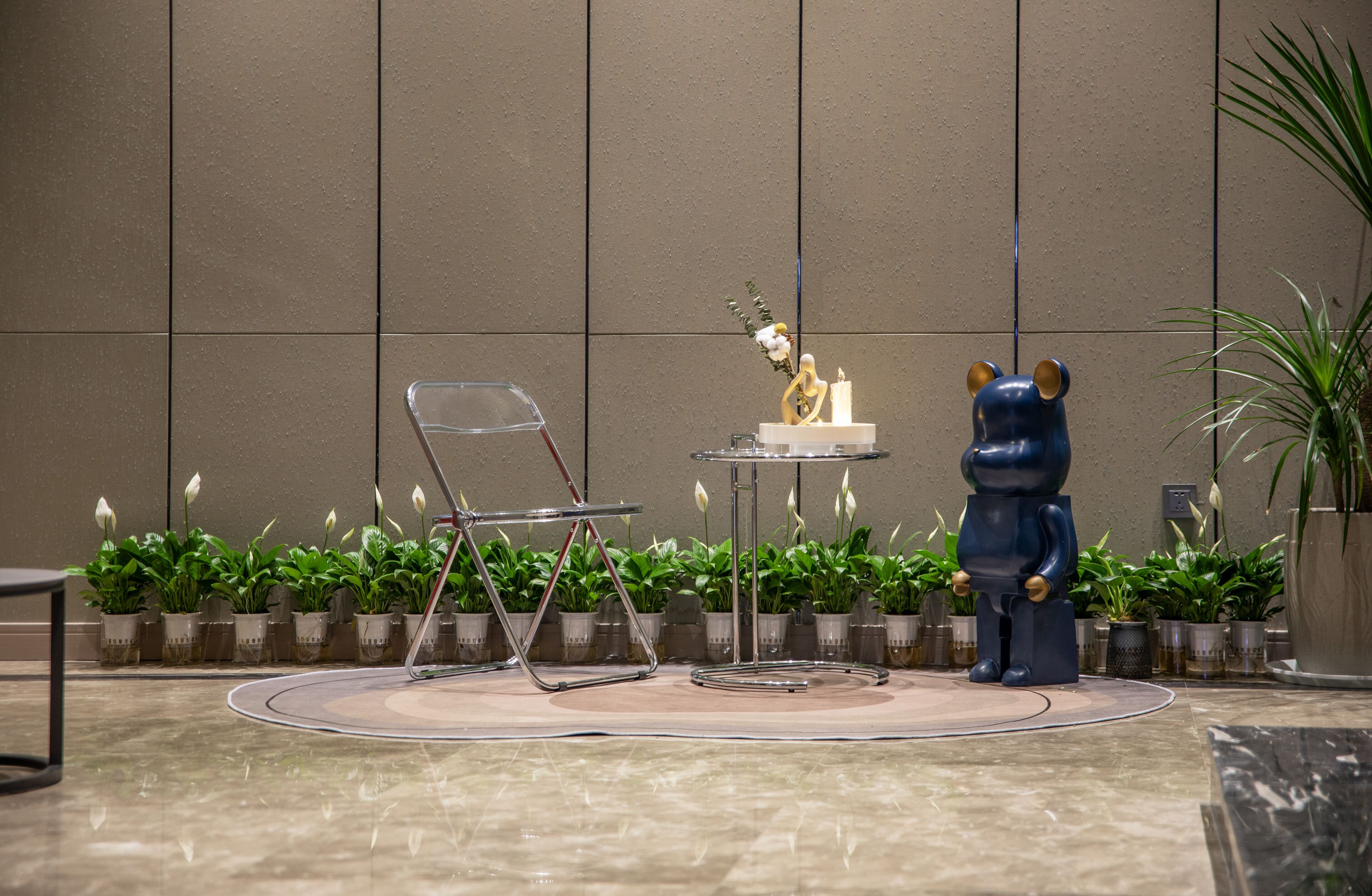 A modern indoor setting with a minimalist design, featuring a clear glass chair, a small table with a decorative item, and a blue bear statue.