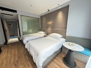 A modern hotel room with a large bed, a bedside table with a cup, and a small round table with a cup. - Yiwu  Manting City Hotel (Jinhua)