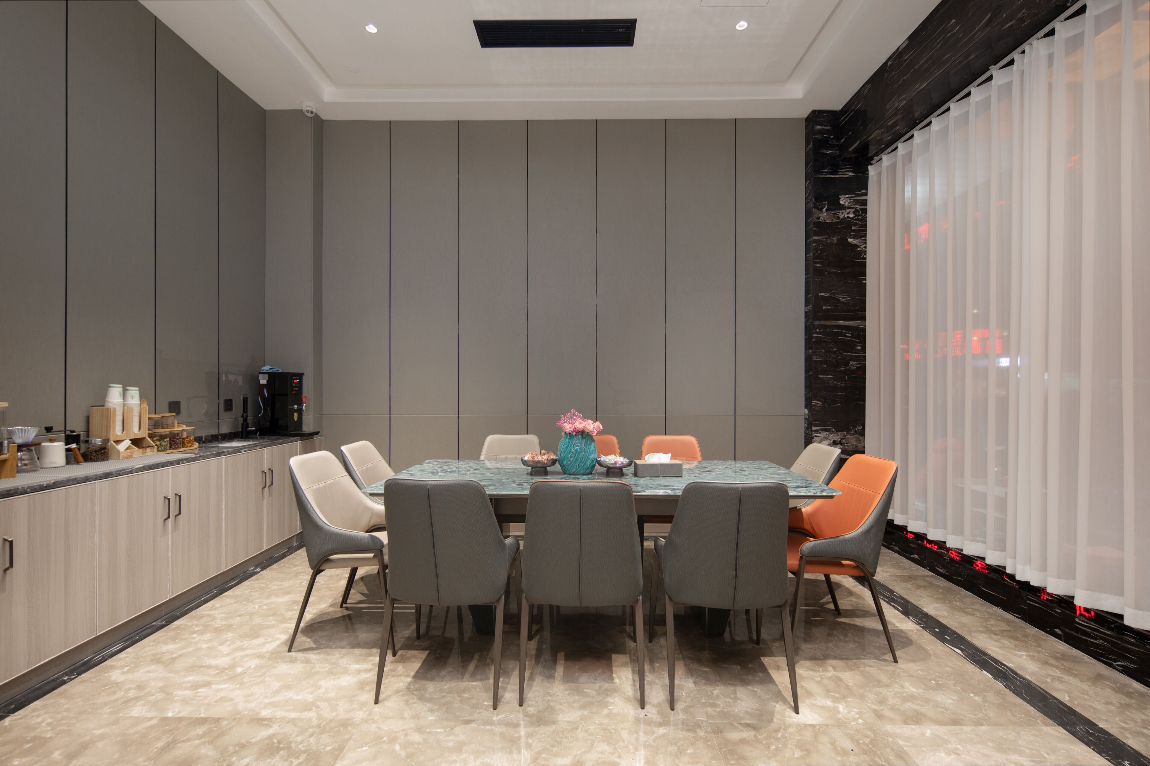A modern dining area with a marble table, grey chairs, and a vase of flowers.
