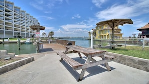 A waterfront promenade with a wooden bench, a dock, and a building with balconies overlooking the water. - Recently remodeled 3br condo at Bay Tree!  Stellar Old Town Port Aransas locatio (Port Aransas)