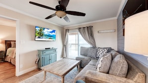 A living room with a ceiling fan, a television, a sofa, a coffee table, and a window with curtains. - Recently remodeled 3br condo at Bay Tree!  Stellar Old Town Port Aransas locatio (Port Aransas)