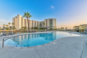 A swimming pool with lounge chairs and a palm tree, surrounded by a fence and buildings. - Bay Tree B11/12 offers a top notch location near the community pool, lighted fis (Port Aransas)