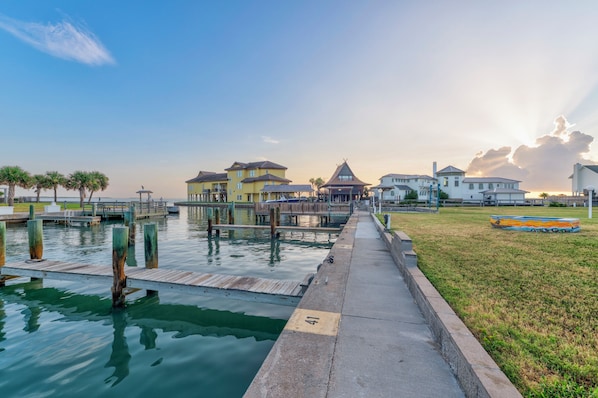 A waterfront property with a dock, a grassy area, and buildings with a mix of architectural styles. - Awesome Bay Tree with a community pool, private lighted fishing pier, boat parki (Port Aransas)