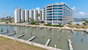 A modern hotel with multiple floors, a marina with docks, and a clear view of the water. - Split-level 2-bedroom rental with access to a pool, tennis courts, fishing pier, (Port Aransas)