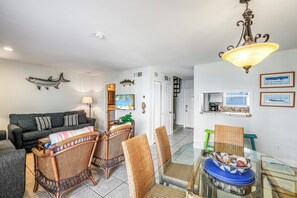 Uma sala de estar com sofá, cadeiras de vime, uma mesa de jantar de vidro e um enfeite de parede com tema de peixes.