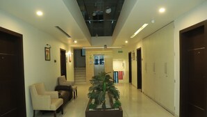 A hotel lobby with a reception desk, seating area, and a central plant. - K Plus Comforts (Karwar)