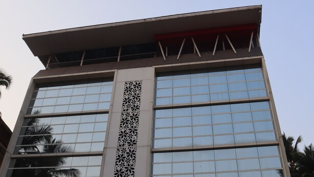 A modern building with a glass facade and a decorative vertical panel. - K Plus Comforts (Karwar)