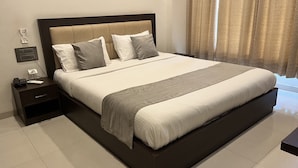 A neatly made bed with a headboard, a bedside table with a phone and a lamp, and a power outlet on the wall. - K Plus Comforts (Karwar)