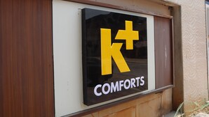 A sign with a large yellow 'K+' symbol and the word 'COMFORTS' below it. - K Plus Comforts (Karwar)