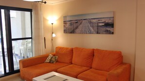 A living room with an orange sofa, a white coffee table, and a painting of a beach scene on the wall. - DORASAL bl.A bajo Solo Familias! (Xeraco Playa)