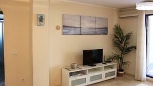 A living room with a flat-screen TV on a white entertainment unit, a large seascape painting on the wall, and a potted plant. - DORASAL bl.A bajo Solo Familias! (Xeraco Playa)