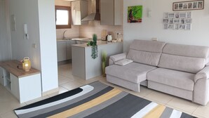 A modern living room with a beige sofa, a kitchen area with a window, and a dining table. - Xeresa del Monte 85 Only Families! (Xeresa)