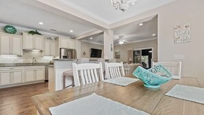 Un vaste espace dédié à la salle à manger, avec une table en bois, des chaises blanches et un panier de couleur turquoise.