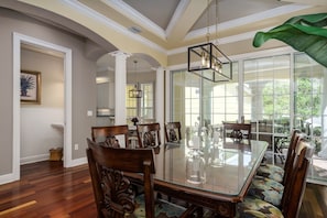 A dining area with a glass table, wooden chairs, and a large window with a view of greenery.