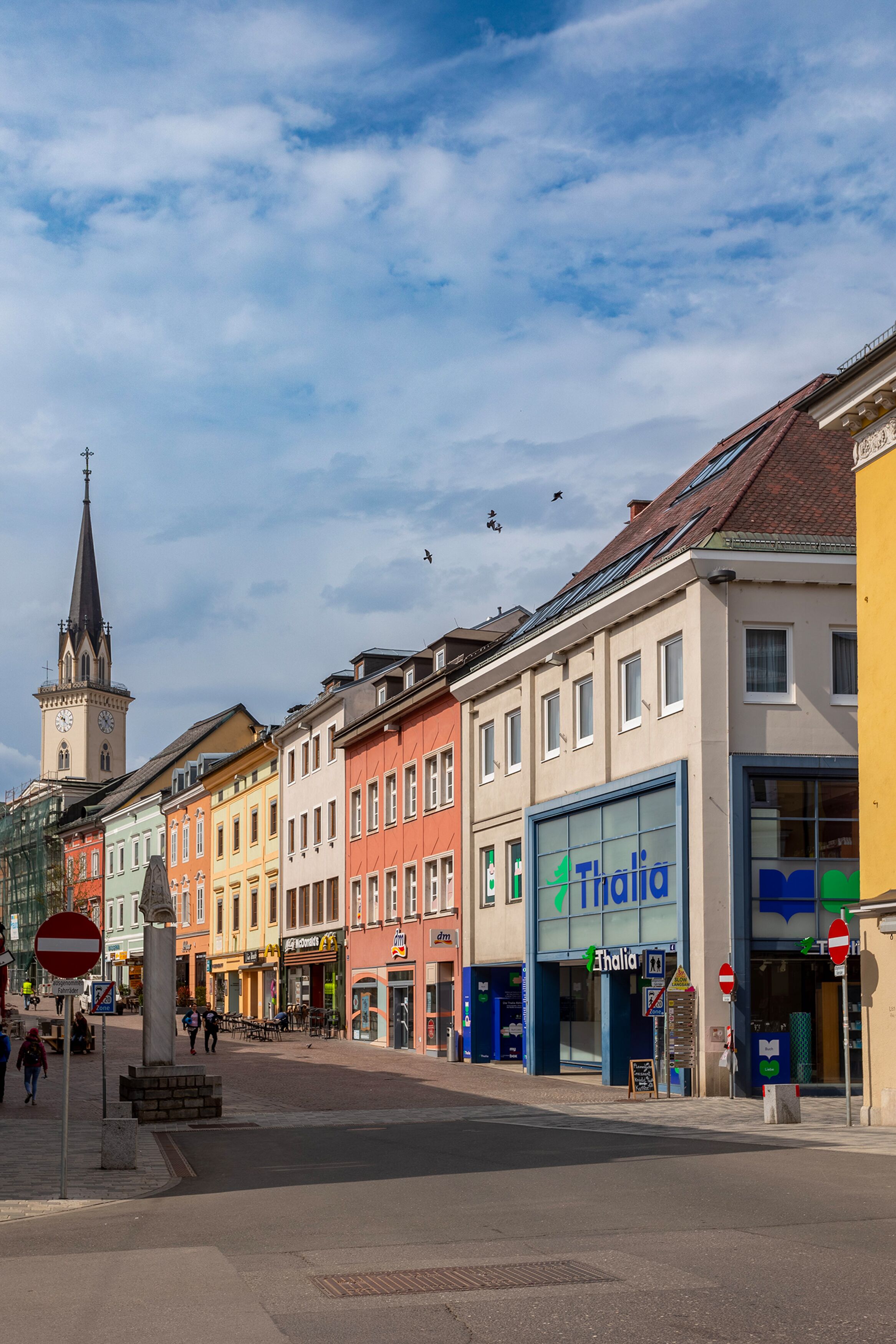 A street with colorful buildings, a clock tower, and a Thalia theater.