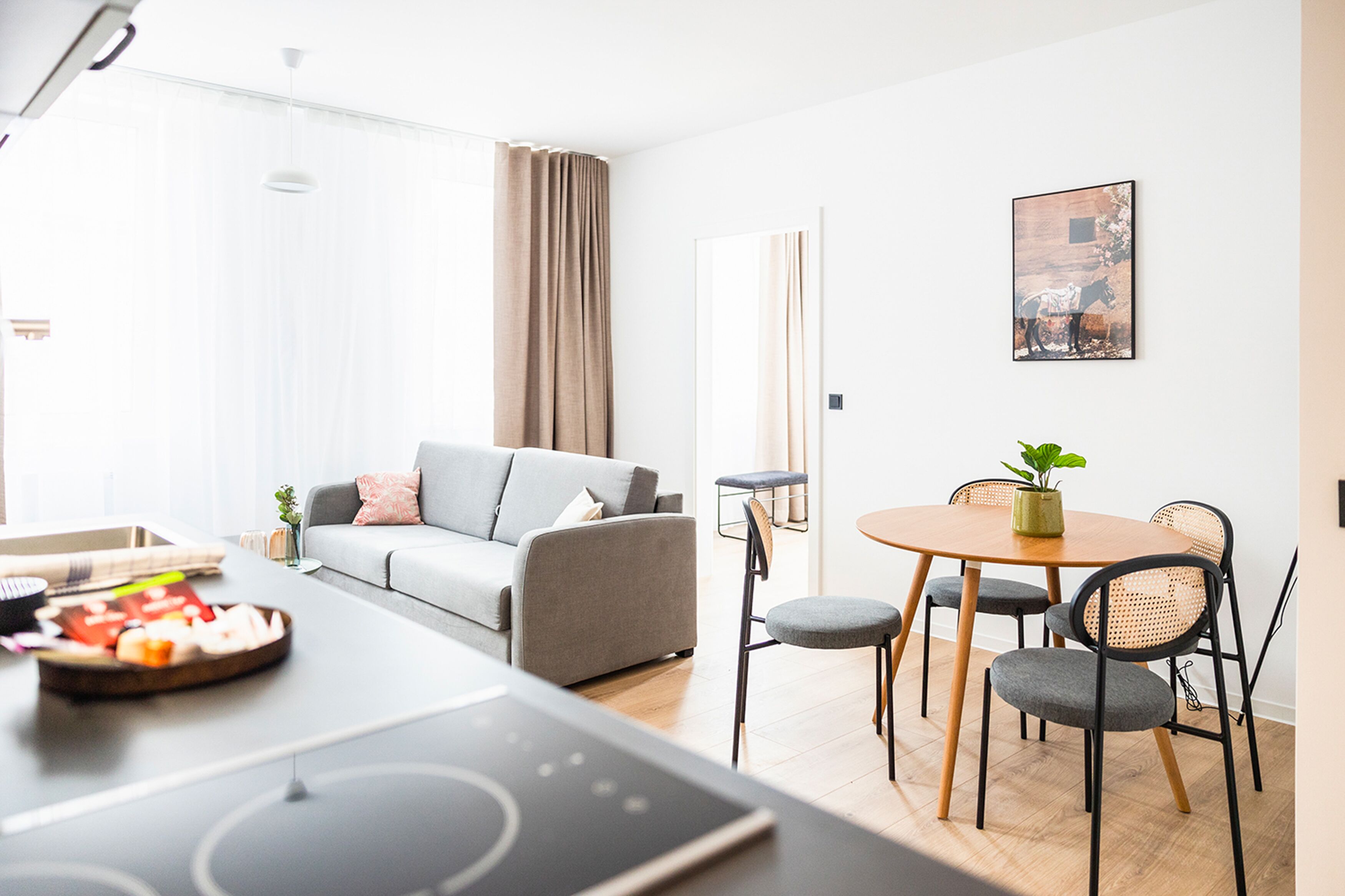 A modern living room with a grey sofa, a dining table with chairs, and a kitchen area with a stove.