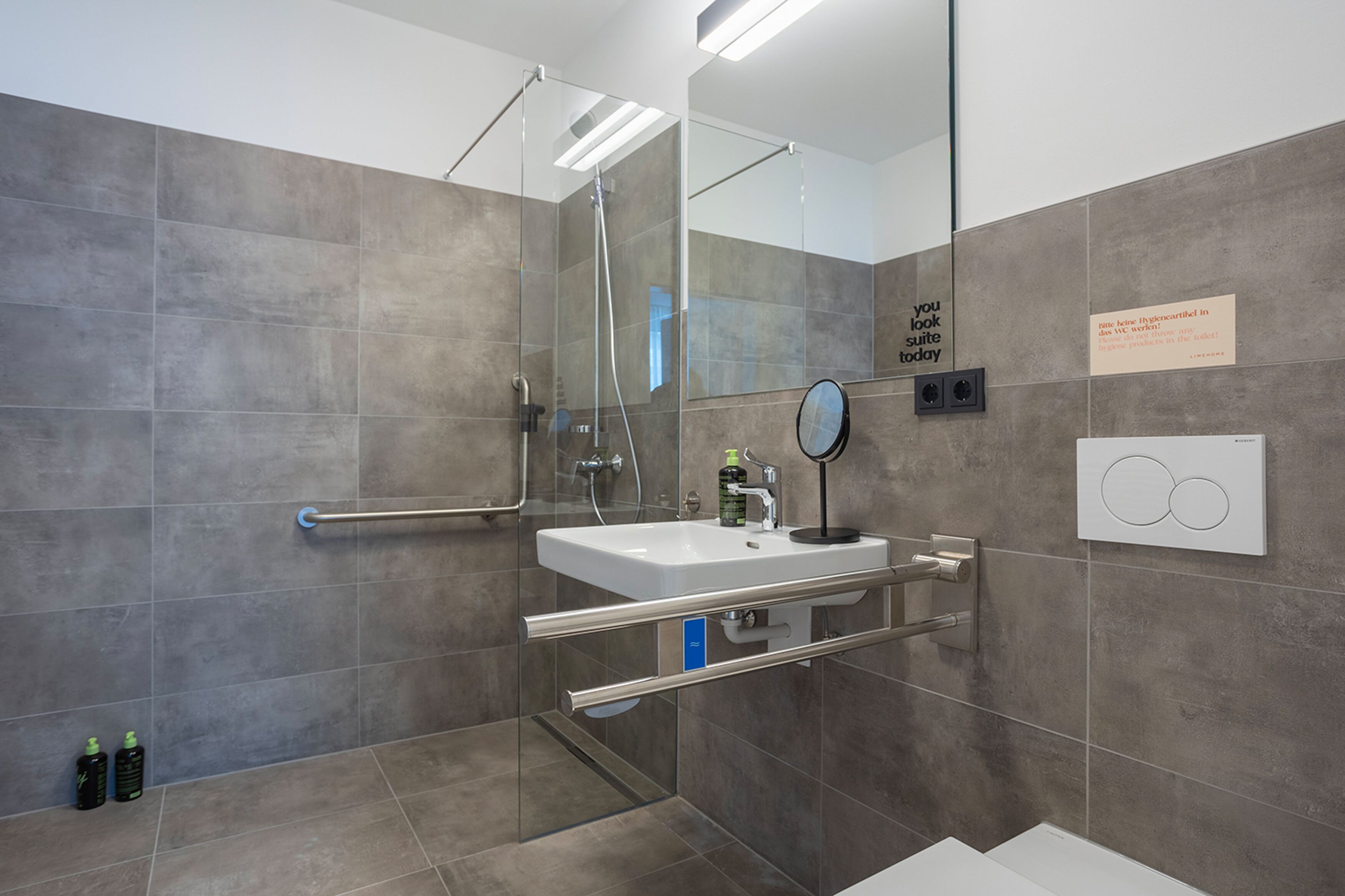 Un baño moderno con ducha envuelta en vidrio, un lavamanos blanco con espejo y un perchero para toallas.
