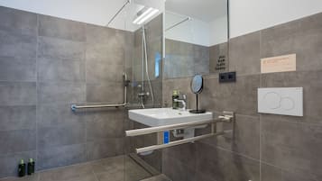 Un baño moderno con ducha envuelta en vidrio, un lavamanos blanco con espejo y un perchero para toallas.