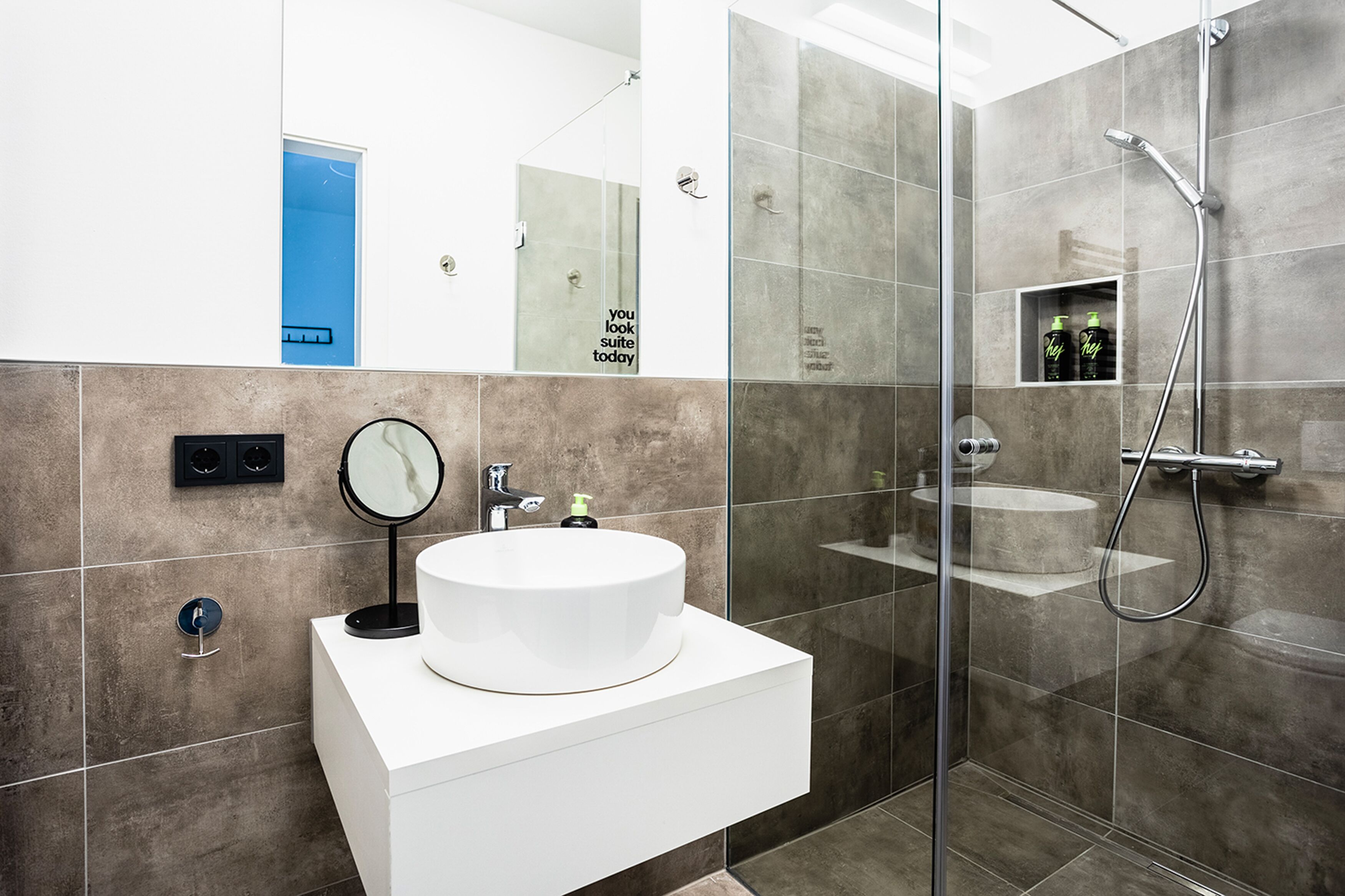Ein modernes Badezimmer mit einem weißen Waschbecken, einer Duschkabine aus Glas und einem Spiegel.