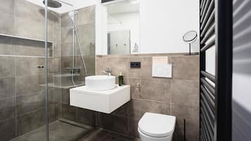 A modern bathroom with a glass-enclosed shower, a white sink, and a toilet.
