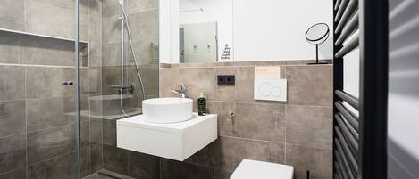 A modern bathroom with a glass-enclosed shower, a white sink, and a toilet.