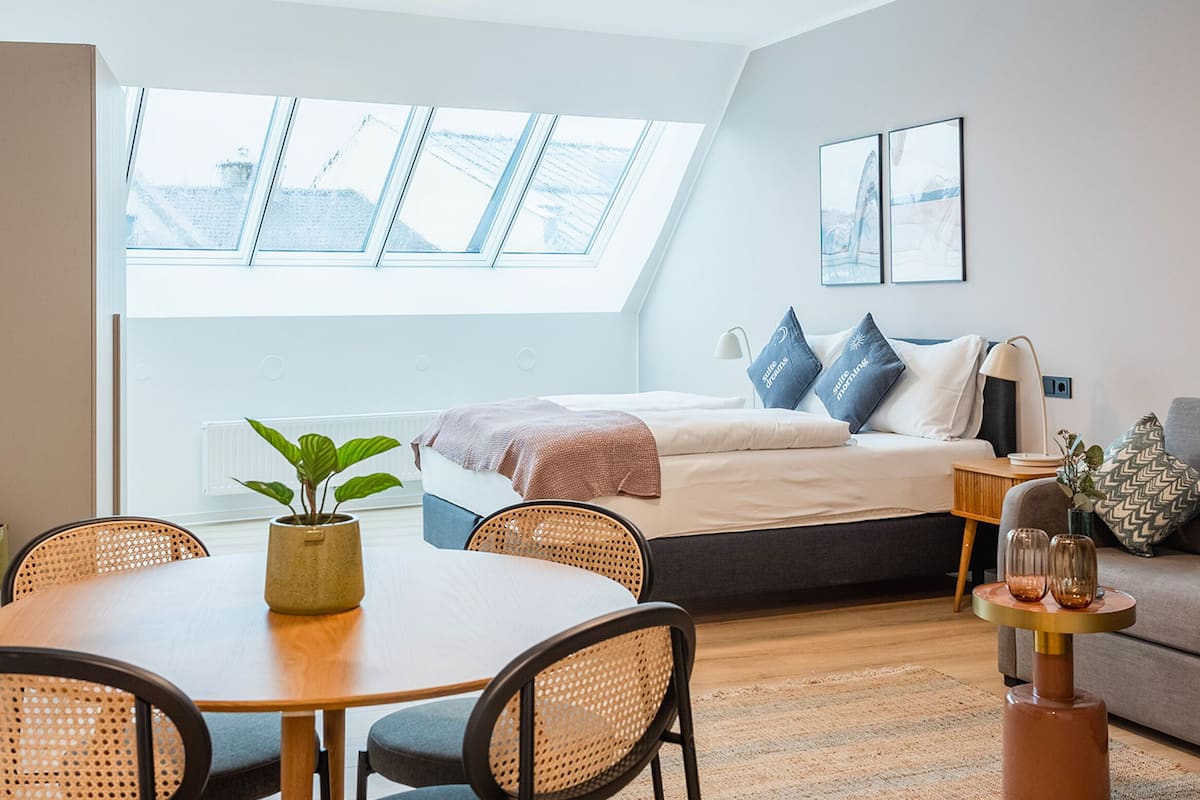 Quarto moderno com claraboia, uma cama com almofadas, uma mesinha de cabeceira e uma pequena planta.