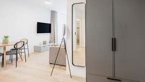 Moderni huone, jossa on harmaa vaatekaappi, työpöytä tuoleineen, seinälle asennettu televisio ja suuri peili.