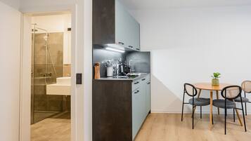 A compact kitchen with a modern design, featuring a built-in oven, a sink, and a dining area with a table and chairs.
